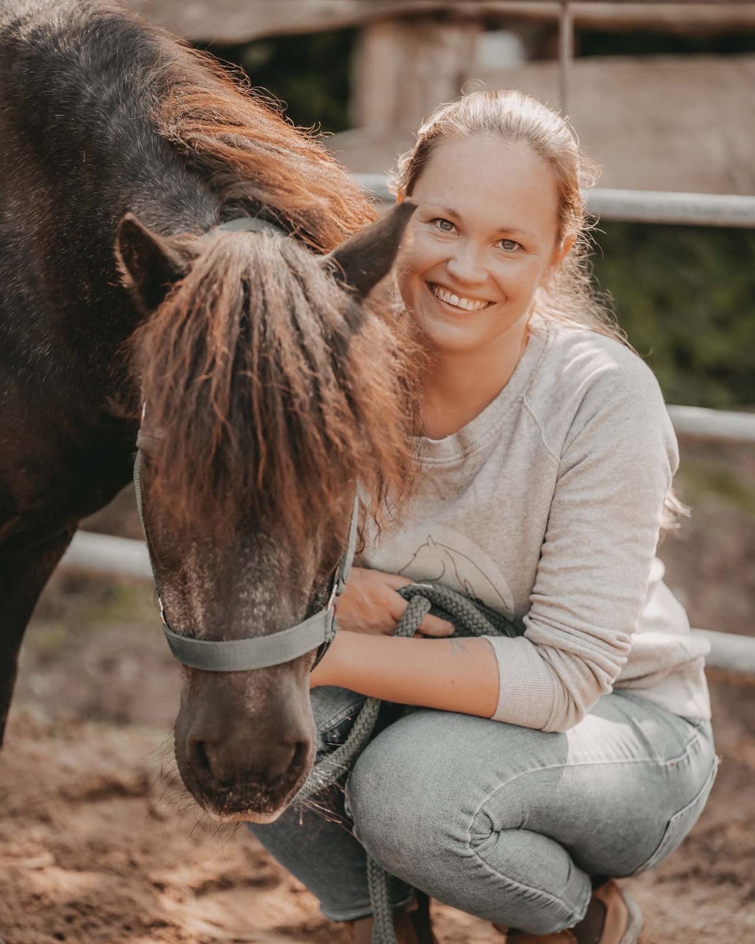 Talitha Gerlach, Dozentin, kniet neben einem dunklen Pferd